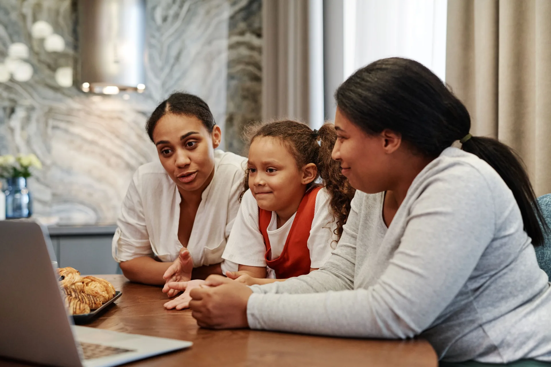 A mother and two children at a kitchen table talking with a clinician on a laptop video call